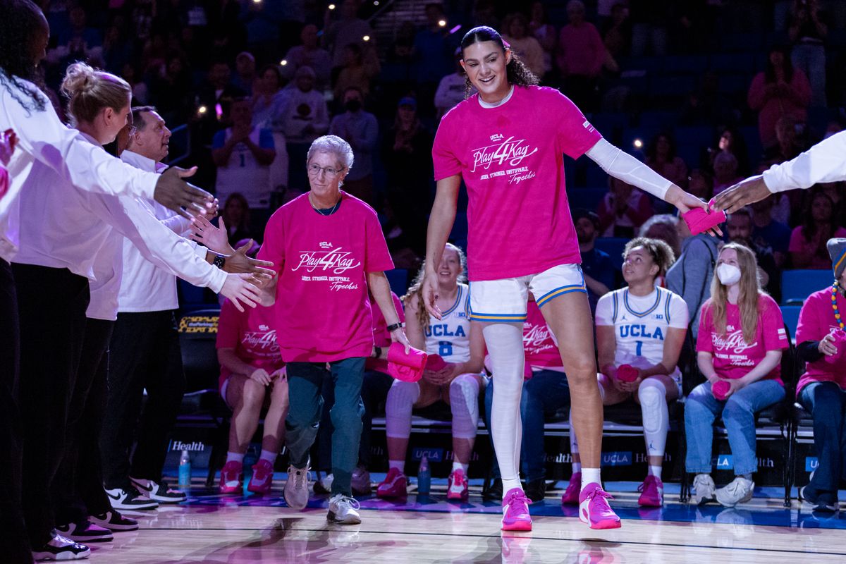 A cancer survivor joins Lauren Betts #51 of the UCLA Bruins for the starting lineup introductions before the Play4Kay Pink game supporting the fight against all cancers affecting women, February 15, 2026 in Los Angeles, Calif.