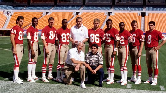San Francisco 49ers head coach Bill Walsh (bottom left) and Eddie DeBartolo Jr. (bottom right) pose with quarter backs and receivers including with Steve Young (8), Joe Montana (16), John Taylor (82), Jerry Rice (80), and assistant coach Mike Holmgren (center)during Super Bowl XXIII media day at Joe Robbie Stadium. 